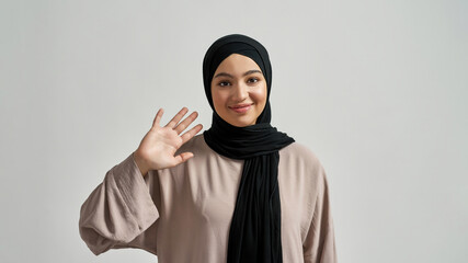 Happy young arabian woman in hijab waving hand