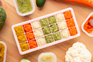 Top view of bowls with healthy baby food in ice cube trays ready for freezing on wooden background..Pureed baby food make by carrot, broccoli and pumpkin