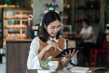Young Asian woman sitting relax at holding a pen coffee shop using a tablet.