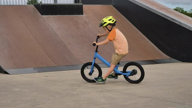 Little boy riding a balance bike in a skatepark, wearing a helmet for safety, almost fall down, crash