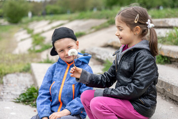 A little girl and a boy look at a dandelion together.