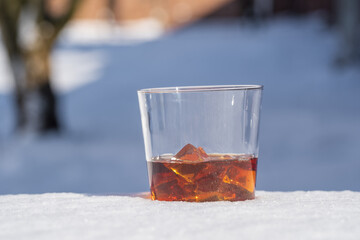 Glass of whiskey with ice on a bed of snow and white background, close up