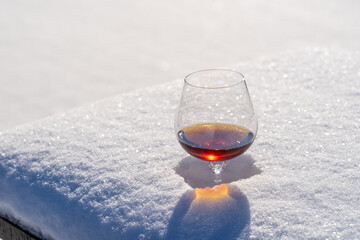 Glass of cognac on a bed of snow and white background, close up
