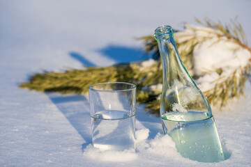 Glass bottle and glass of water on a white snow in winter