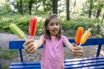 Little girl eating colorful ice cream sitting on a bench.