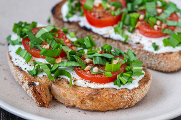 Delicious toasted bread with white cream cheese, green wild garlic and tomato on plate, close up