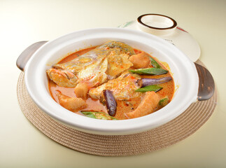 chef cook home style nyonya spicy curry grouper fish head with vegetables in big clay pot on white table restaurant asian cafe halal chinese banquet menu