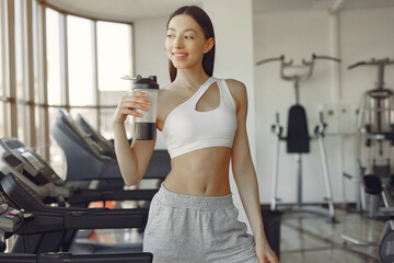 Fototapeta premium A beautiful girl standing in a gym with bottle of water