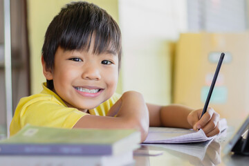 Portrait image of 7-8 years old kid. Happy Asian student child boy using and touching smart pad or tablet for do his homework and online learning (E-learning). Back to school, Study frome home.