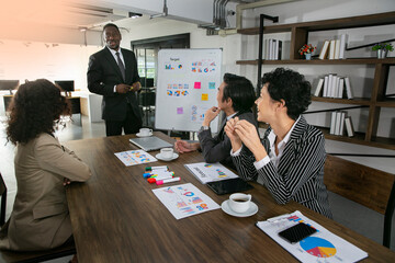 African American Manager briefting the the department goal to his team. On the table contain a pile chart and graph that using for their meeting. Business meeting concept.