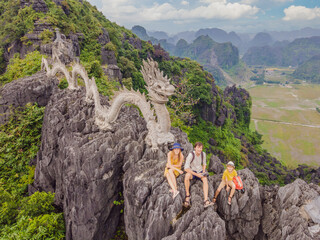 Family of tourists on the background of Amazing huge dragon statue at limestone mountain top near Hang Mua view point at foggy morning. Popular tourist attraction at Tam Coc, Ninh Binh. Vietnam travel