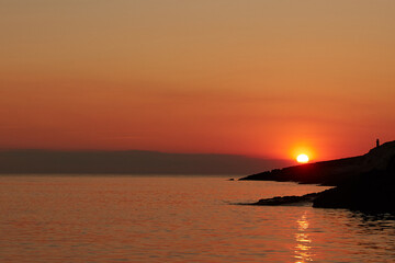 Silhouette of a woman watching sunset over distant horizon.