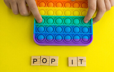 Close-up of children's hands bursting bubbles in the popular pop it game. Children's entertainment pop it. Inscription pop it in wooden letters. selective focus, shallow depth of field.