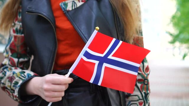 Unrecognizable Woman Holding Norwegian Flag. Girl Walking Down Street With National Flag Of Norway