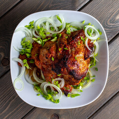 Top view of baked pork neck meat with green onions and rings on a white plate on a wooden background.