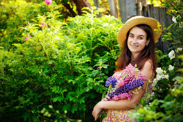 A beautiful pregnant young woman in a straw hat with a bouquet of pink and lilac flowers in her hands.