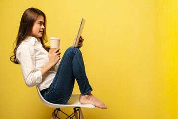 Women playing tablet while drink coffee sitting on chair with yellow background