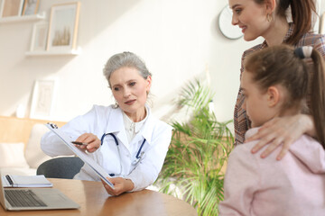 Fototapeta premium Mother and child in the doctor office meeting the pediatrician, they are sitting at desk in hospital.