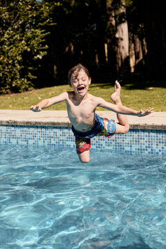 Expressive child jumping into pool water on sunny day