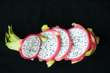 Slices of dragon fruit or pitaya with pink skin and white pulp with seeds on black background....