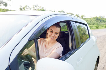 smiling woman driver is sitting in her car, window is open, woman is looking at camera