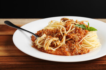 Close up a fork with spaghetti and red sauce in white dish on cutting board