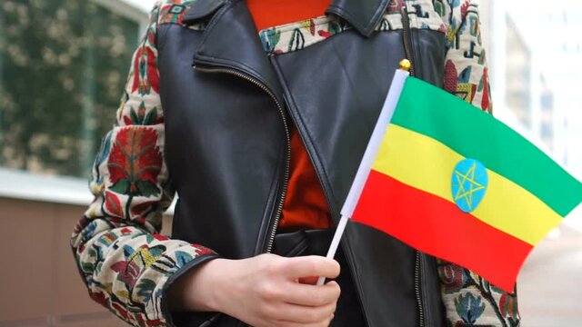 Unrecognizable woman holding Ethiopian flag. Girl walking down street with national flag of Ethiopia