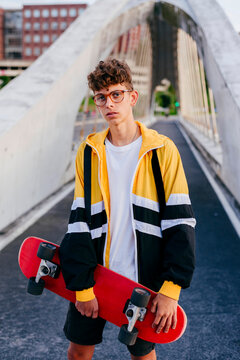 Caucasian teenager with skateboard standing on the bridge in the city