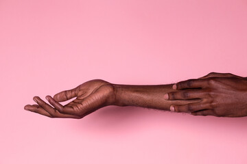 Black man touching his forearm with hand on pink background