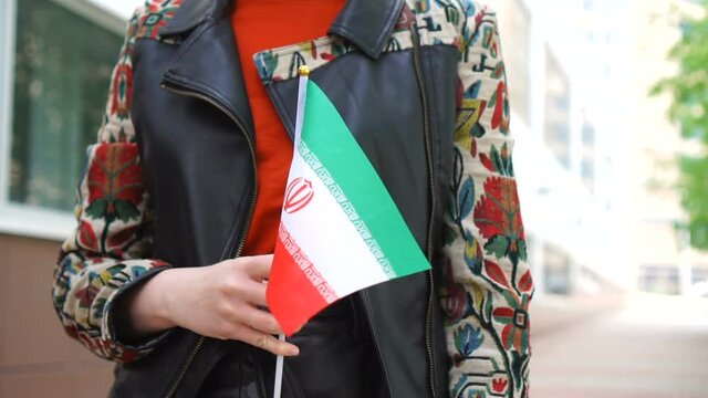 Unrecognizable woman holding Iranian flag. Girl walking down street with national flag of Iran