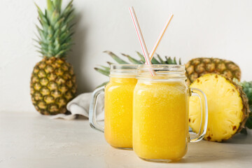 Mason jars of tasty pineapple smoothie on light background