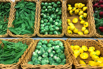 Fresh Brussel sprouts, green peas, yellow squash patty pan patisson piled in the baskets on the market. Food background.