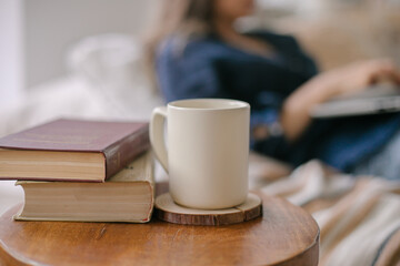 Vintage books with coffee cup or mug on wooden table against the background of a girl working at a laptop. Place for text, design. mockup