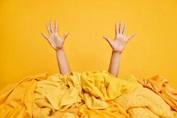 Unrecognizable human raised arms up poses near pile of laundry against vivid yellow background....