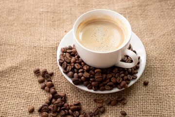 Cup of fresh brewed coffee with roasted coffee beans on brown cloth background.