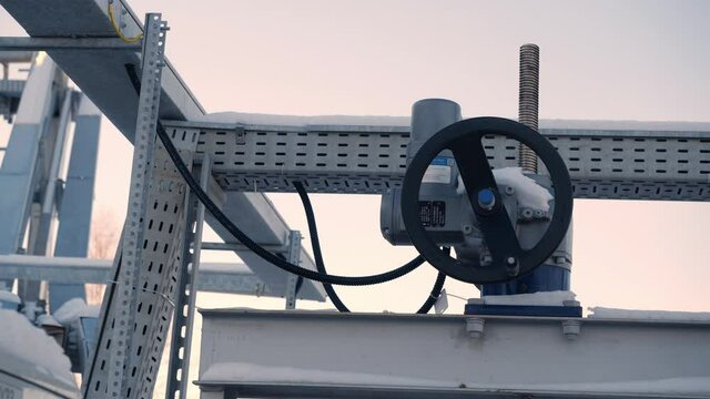 Black round lever on metal construction under cloudy sky at large purification station at sunset light on winter close view