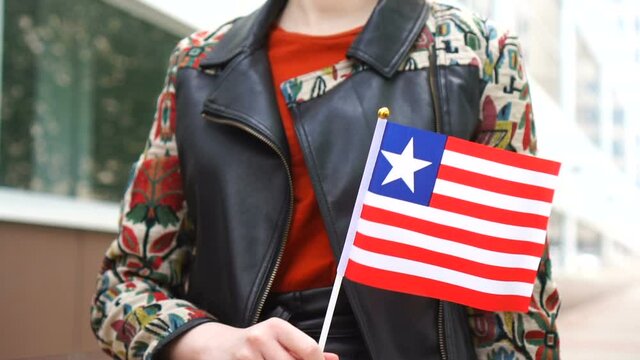 Unrecognizable woman holding Liberian flag. Girl walking down street with national flag of Liberia