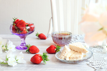 The concept of good morning. Ripe strawberries, airy waffles, white bells, a cup of tea , a gray napkin on the background of a white wooden chair.
