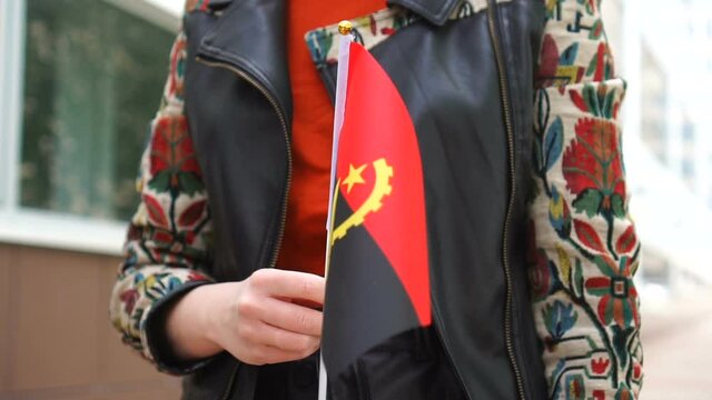 Unrecognizable woman holding Angolan flag. Girl walking down street with national flag of Angola