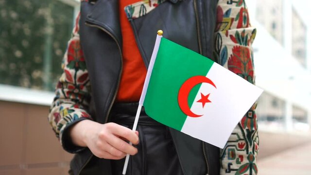 Unrecognizable woman holding Algerian flag. Girl walking down street with national flag of Algeria