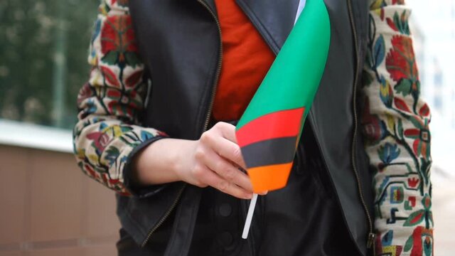 Unrecognizable woman holding Zambian flag. Girl walking down street with national flag of Zambia