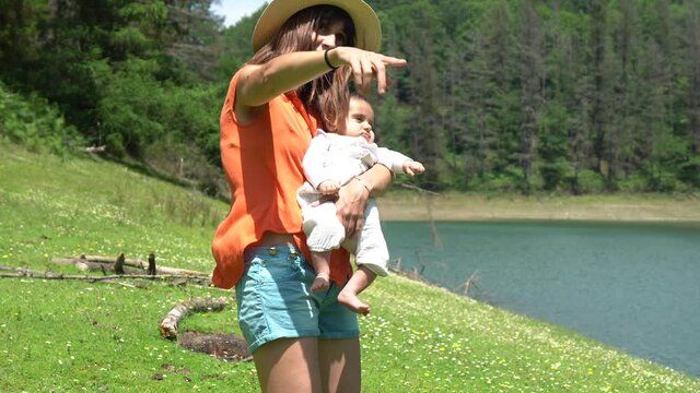A mother teaching nature to her newborn son at a lake surrounded by pine trees and beautiful flowers. A reservoir in Navarra next to Lesaka