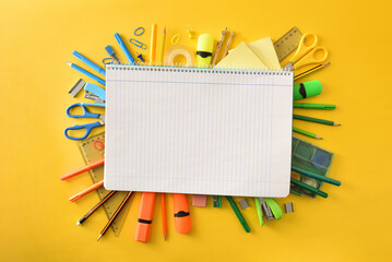 Notebook on pile of school supplies on yellow background