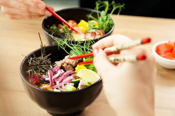 Man and woman eating poke salad with chopsticks. Dab tuna salad in a bowl. People in the restaurant eat salad with chopsticks. Asian seafood salad concept.