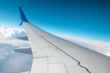 Fototapeta premium A wing of a modern passenger airplane above the clouds. International cargo transportation, air travel, transport. Copy space.