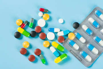 Assorted pharmaceutical medicine pills, tablets and capsules on blue background