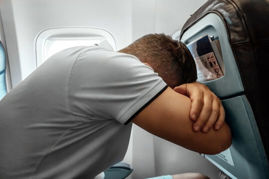 A man sits in front of an airplane window and is nervous, afraid to fly, the cabin of a passenger aircraft. Aerophobia, fobilya, international flights.