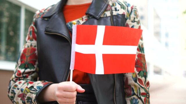 Unrecognizable woman holding Danish flag. Girl walking down street with national flag of Denmark