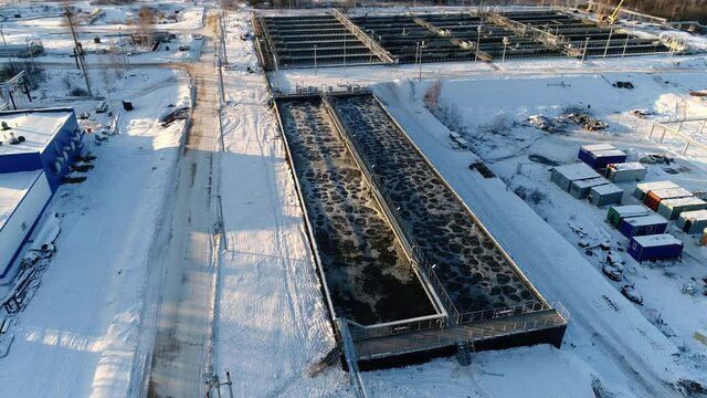 Reservoirs with aerating wastewater and bridge at modern purification station at sunset light in winter evening aerial view