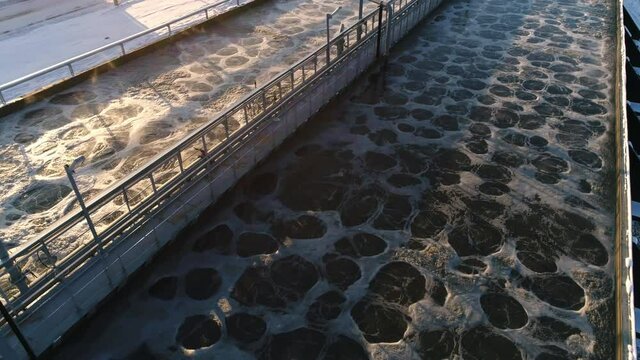 Swirling water in large tanks for aeration at modern treatment station at sunset light in winter evening view from above